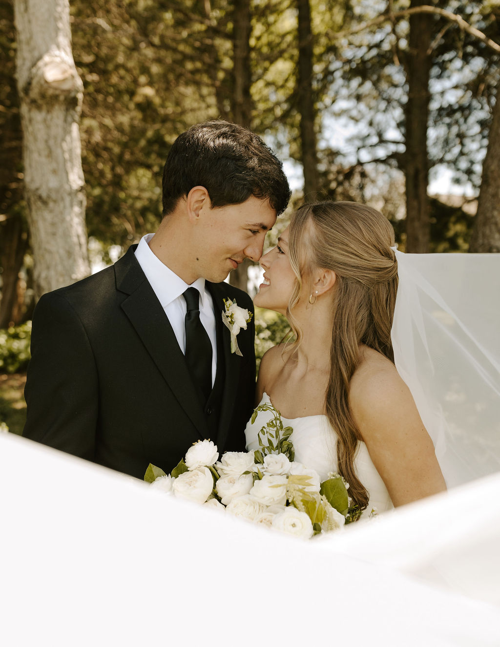 a bride and groom lovingly look at each other while the bride's veil swoops across the photo